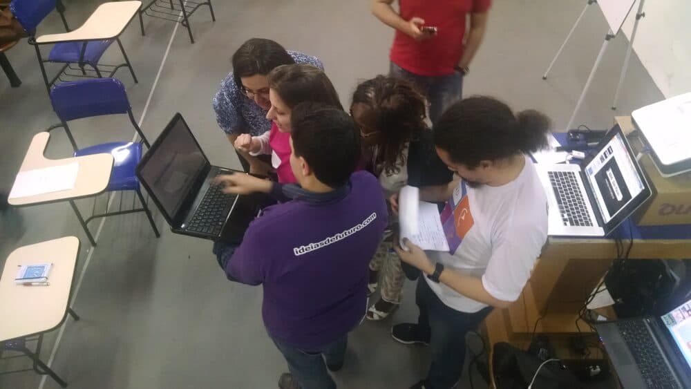 Participantes do Startup in School reunidos em volta de um notebook durante uma atividade.